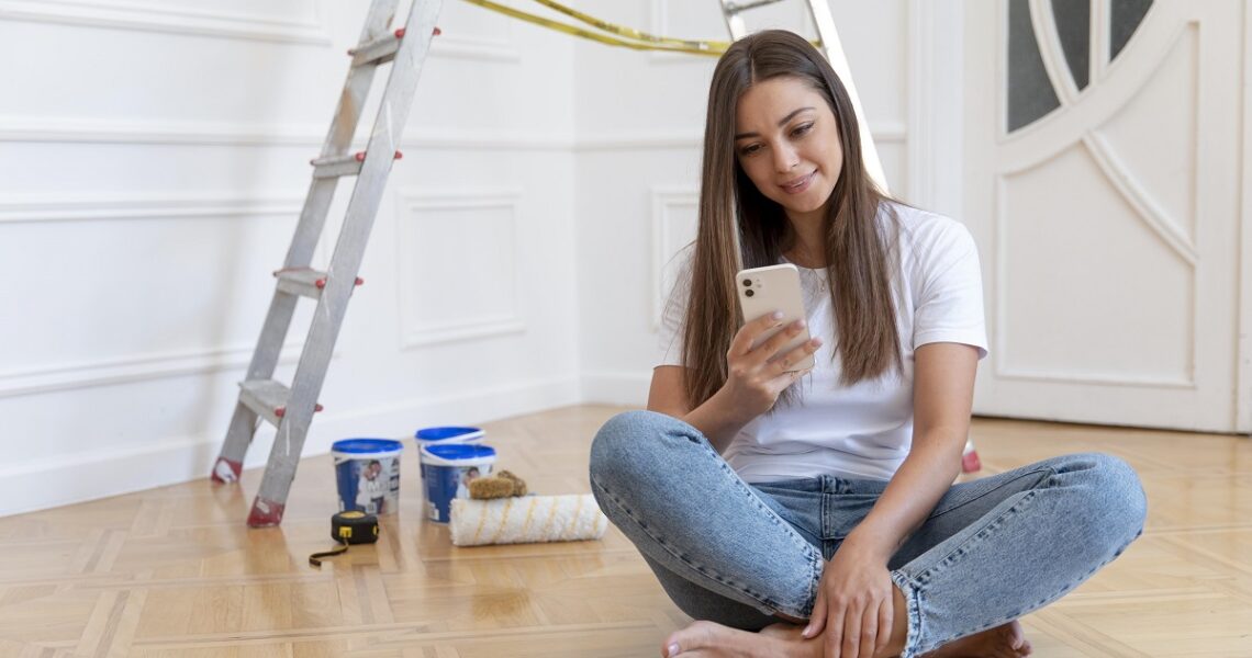 Mulher em reforma do seu apartamento com celular na mão