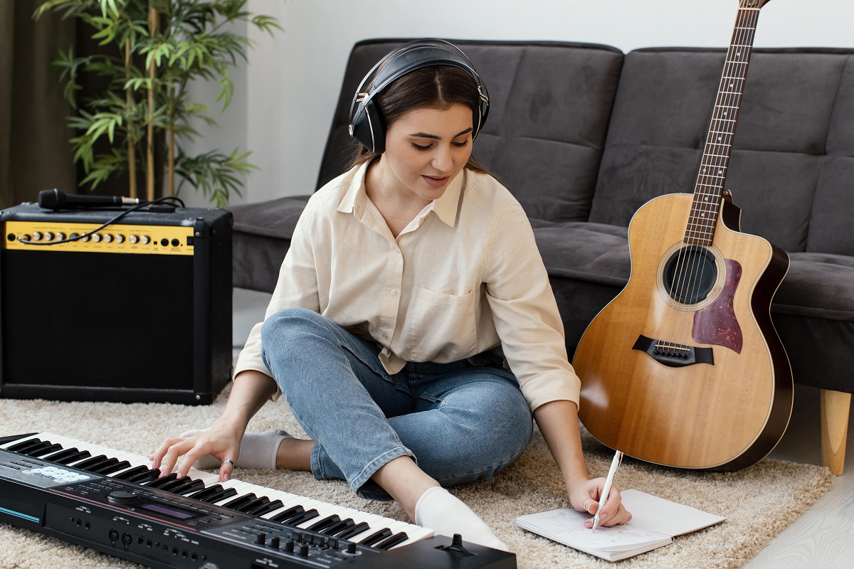 Vista frontal de uma musicista com teclado de piano e violão escrevendo musicais
